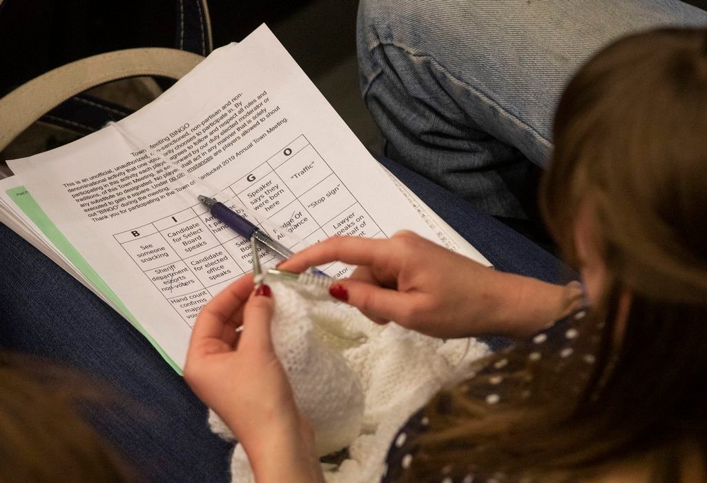 A knitter at Town Meeting keeps track of who said what while playing Harvey Young's Town Meeting Bingo.