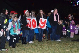 Carolers hold up letters spelling "JOY."