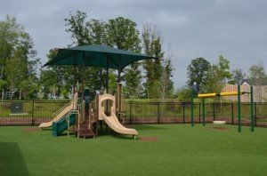 The playground at Primrose school features two slides and a tire swing in a safe gated turf grass yard.  