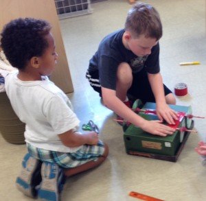Two campers work to create a moving vehicle. 