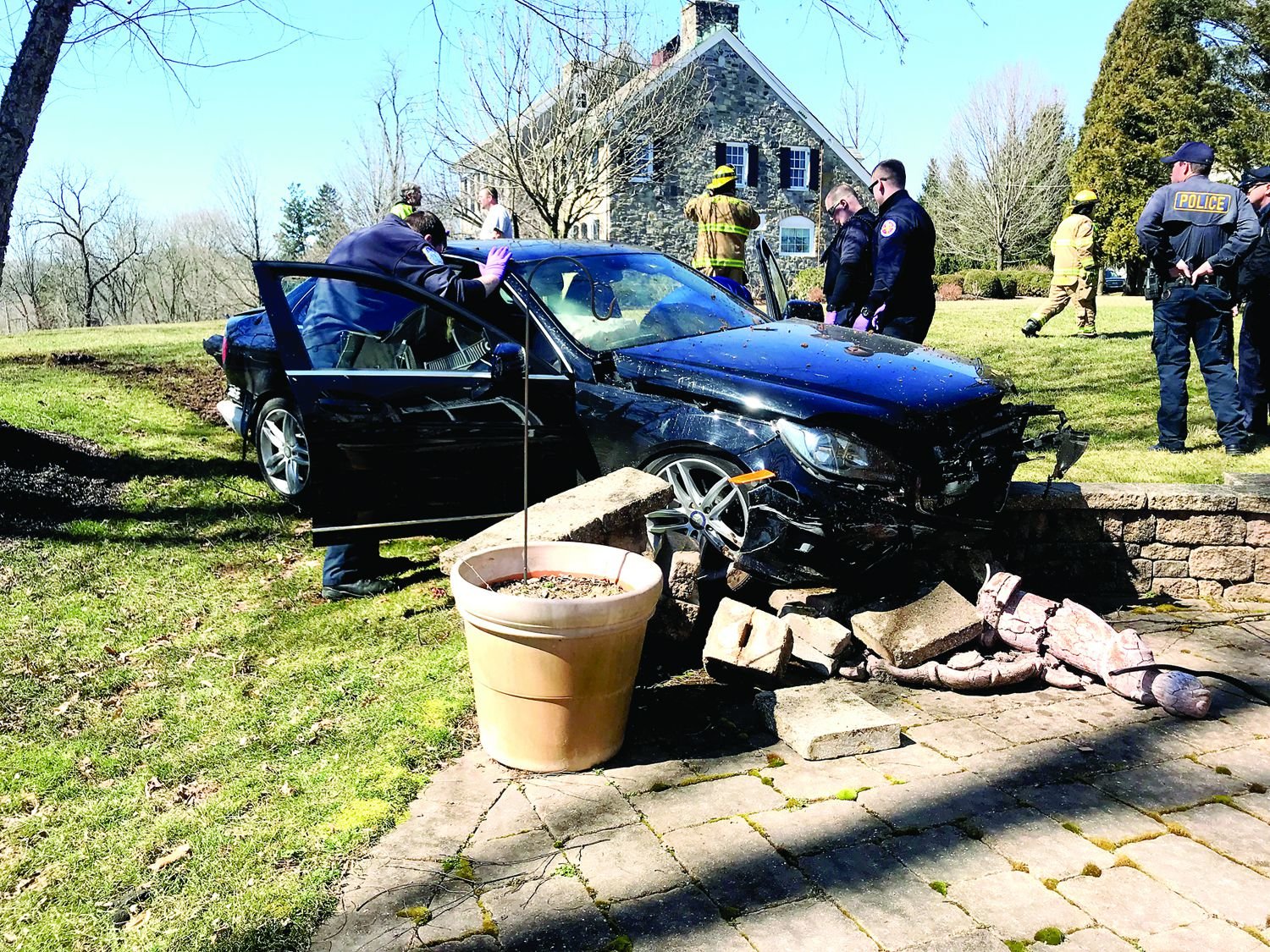 Solebury Police and emergency services crews investigate the scene of a crash that seriously injured two people when this car ran off the road, became airborne and came to rest along a patio wall in Fox Run Preserve. Tire tracks can be seen in the grass behind the car. Photograph by Kristy Smith.