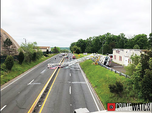 A Plumsteadville Fire Co. ladder truck  is on its side with the ladder extended across Route 611 after it fell during an attempt to reposition an American flag during a Memorial Day commemoration.