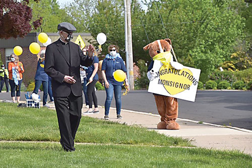 Monsignor Charles H. Hagan waives to well-wishers, and Michelle Stetler, OLMC School, director of Institutional Advancement, wears the school mascot uniform during the socially distanced celebration.