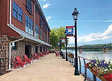 Red Adirondack chairs line the walkway at Ghost Light Inn, with sufficient distancing, along the riverwalk for guests and visitors to enjoy the panoramic views of the Delaware River.