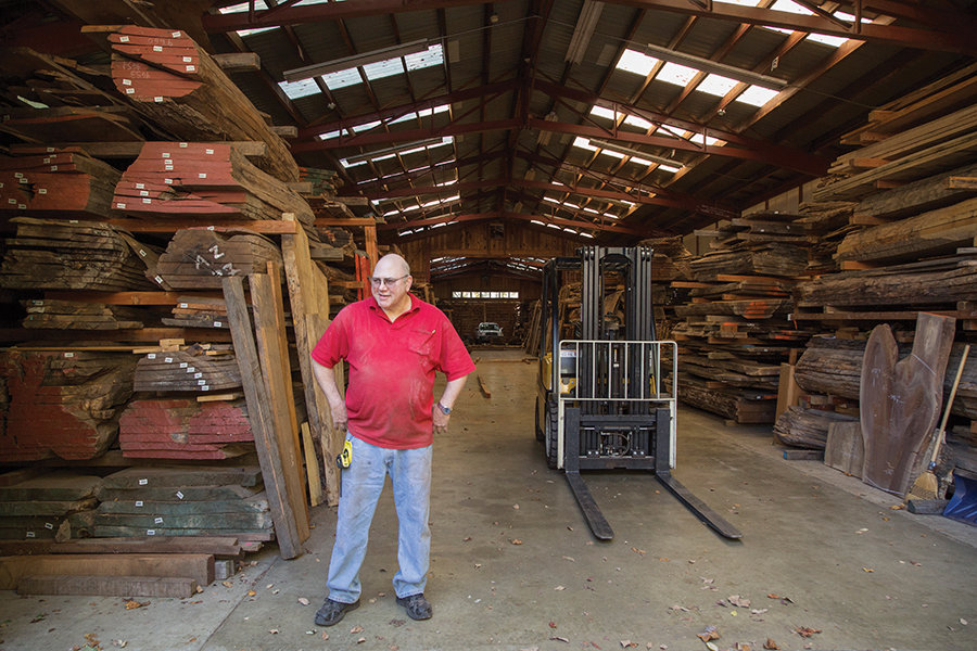 Gerald Everett stands among stacks of walnut and other woods in one of the George Nakashima Woodworkers studio’s lumber sheds.