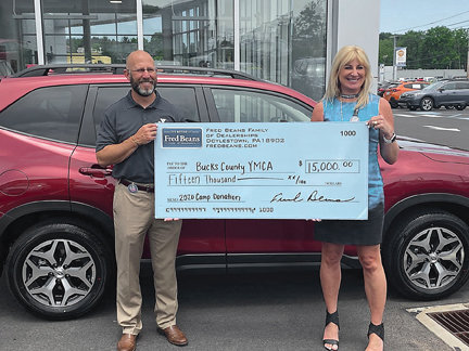 Zane Moore, president/CEO of YMCA of Bucks County, and Beth Beans Gilbert, vice president of the Fred Beans Automotive Group, during a recent check presentation ceremony on the grounds of Fred Beans in Doylestown.