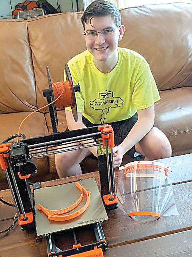 Robostorm 4-H robotics club member Mike Rowe with a 3D printer and face shield pieces made with it.