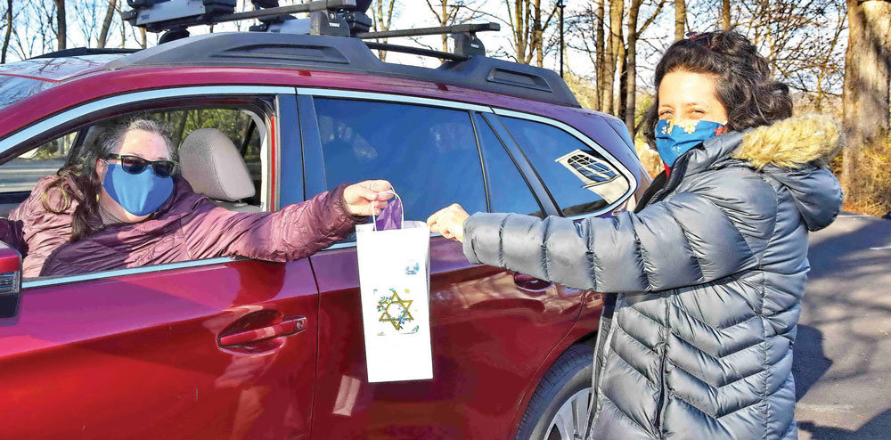 Rabbi Diana Miller hands a kit to Deborah Wean, one of the many members arriving in their vehicles. (Photograph by Gordon H. Nieburg)