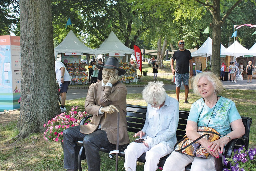 Two women rest on a bench beside a sculpture by Seward Johnson.