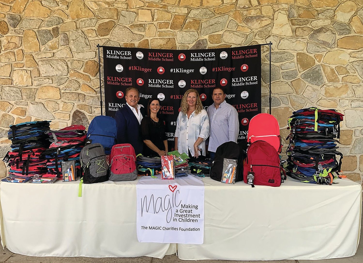 Steve and Sharon Grosso, co-founders of the MAGIC Charities Foundation, Kathy Guzman, marketing consultant for Benchmark Lending, and Glenn M. Davis, branch manager of Benchmark Lending, stand with donated backpacks and school supplies at Klinger Middle School in Southampton.