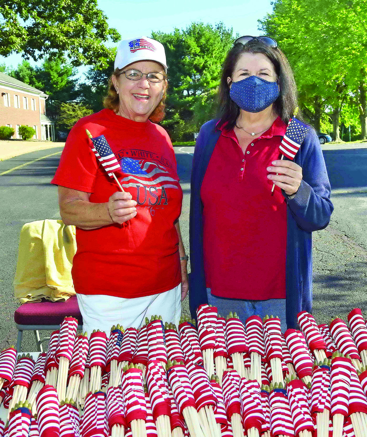 Church members Joyce Linder, left, and Lisa Stuhs hand out the 3,000 American flags to member volunteers.