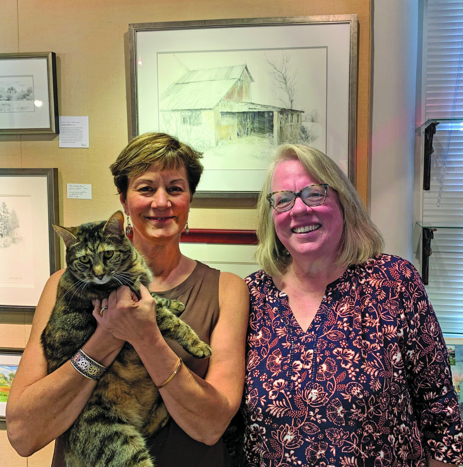 Yvonne Leathead, left, and Lucy the gallery cat celebrate the final transfer of Simons Fine Art to Jane Ramsey.