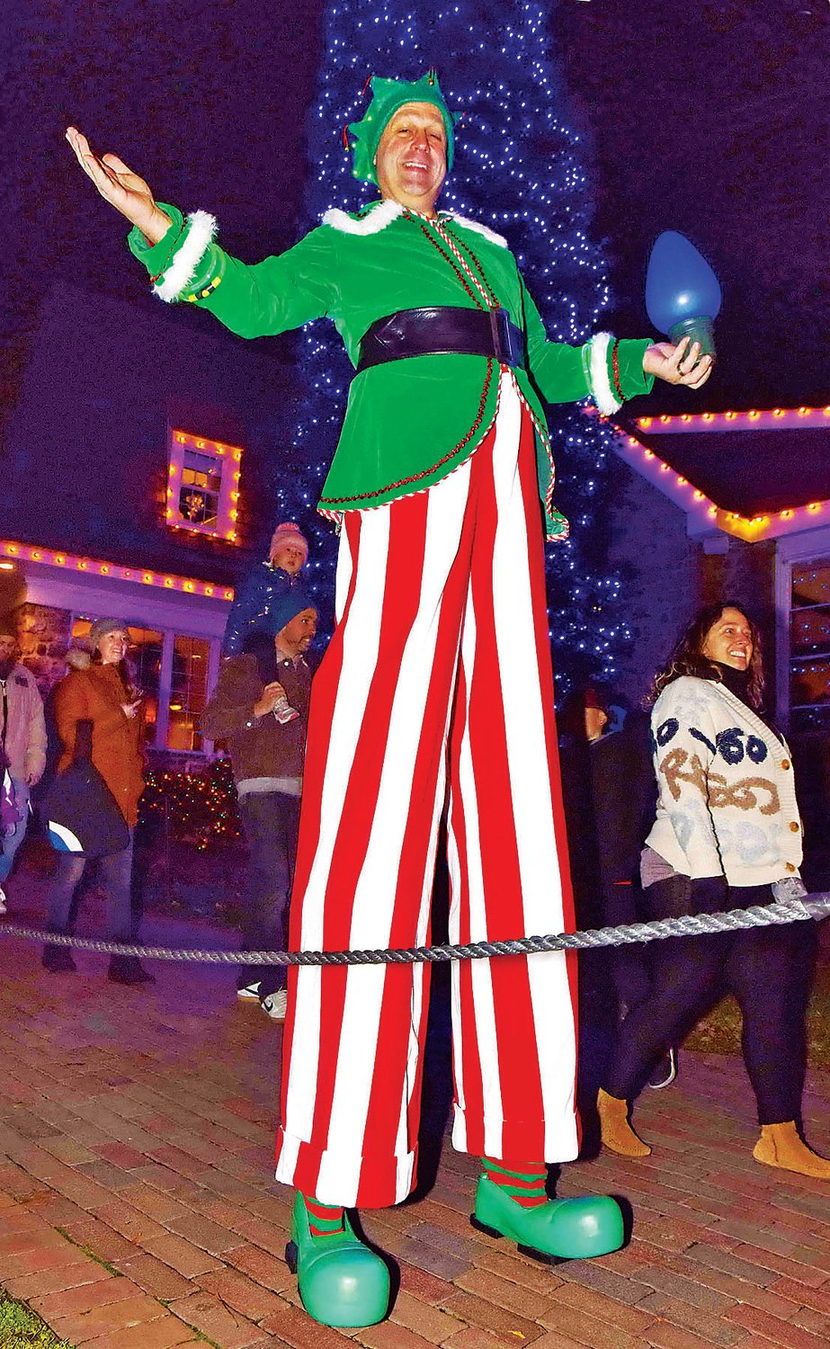 A holiday entertainer walks with guests through the lighting displays.