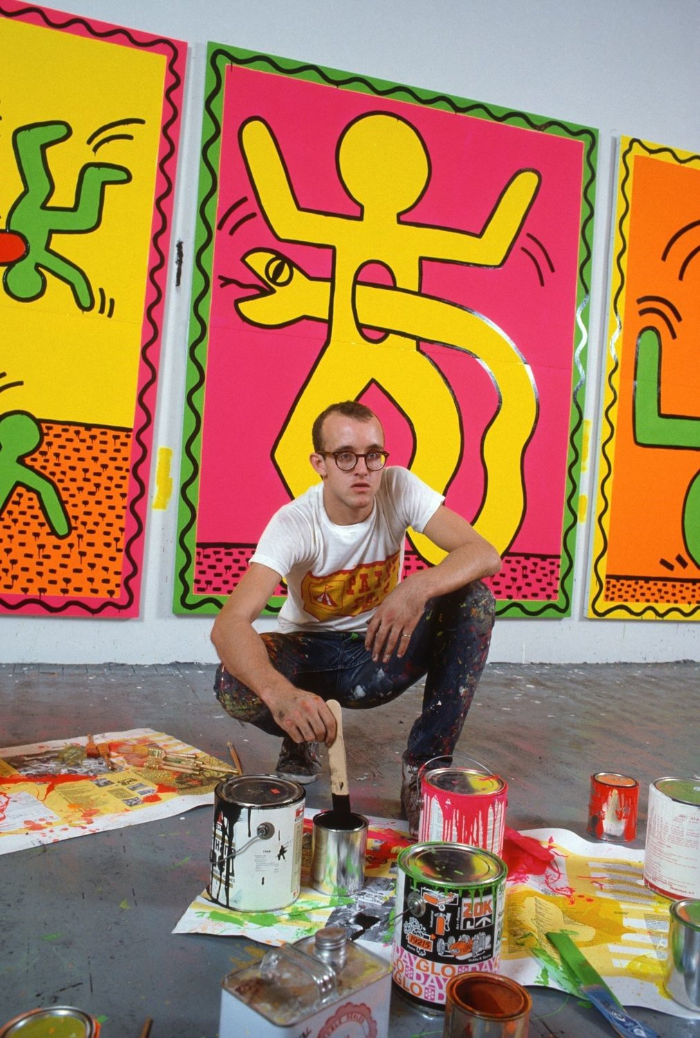 Keith Haring (1958-1990), at work, with some of his recognizable creations behind him.
