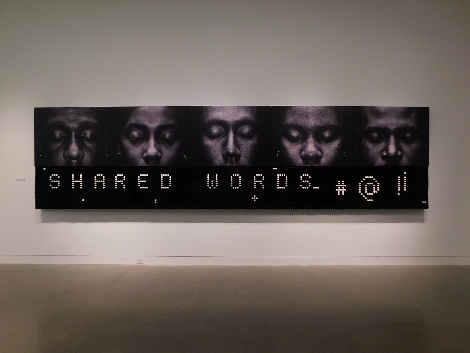 “Shared Words” by Alexandre Arrechea features five black and white portraits printed on an aluminum sheet mounted above a scoreboard-like acrylic grid covering the subjects’ mouths. Visitors are invited to give voice to those depicted by spelling words with sticks of white chalk.