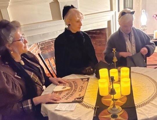 Amy Hollander, acting as a medium at a Victorian Age séance, prepares her Ouija board and waits for others to join her circle, before donning a black veil and channeling the spirit of Col. Arthur Erwin.