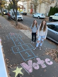 A crew of 18 Chalk Ninjas decorated town sidewalks with reminders to vote before or on Election Day, Tuesday, November 8. Pictured are two of the ninjas, Lucy Spreen, left, and Ava Duggan, right.