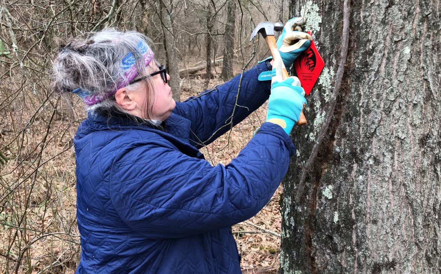 Debbie Kratzer nails a trail marker to a tree at Muddy Run Preserve. The trail is named in honor of her husband, Todd Kratzer, who passed away in 2012.