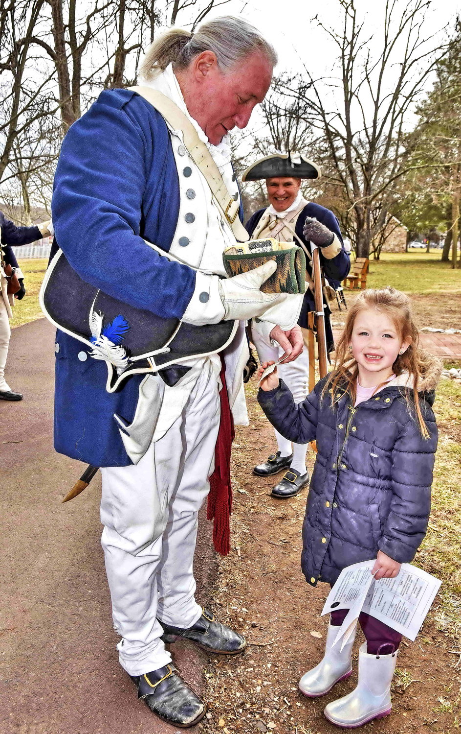 A soldier presents replica Colonial currency to Brantley McCoy, 5.
