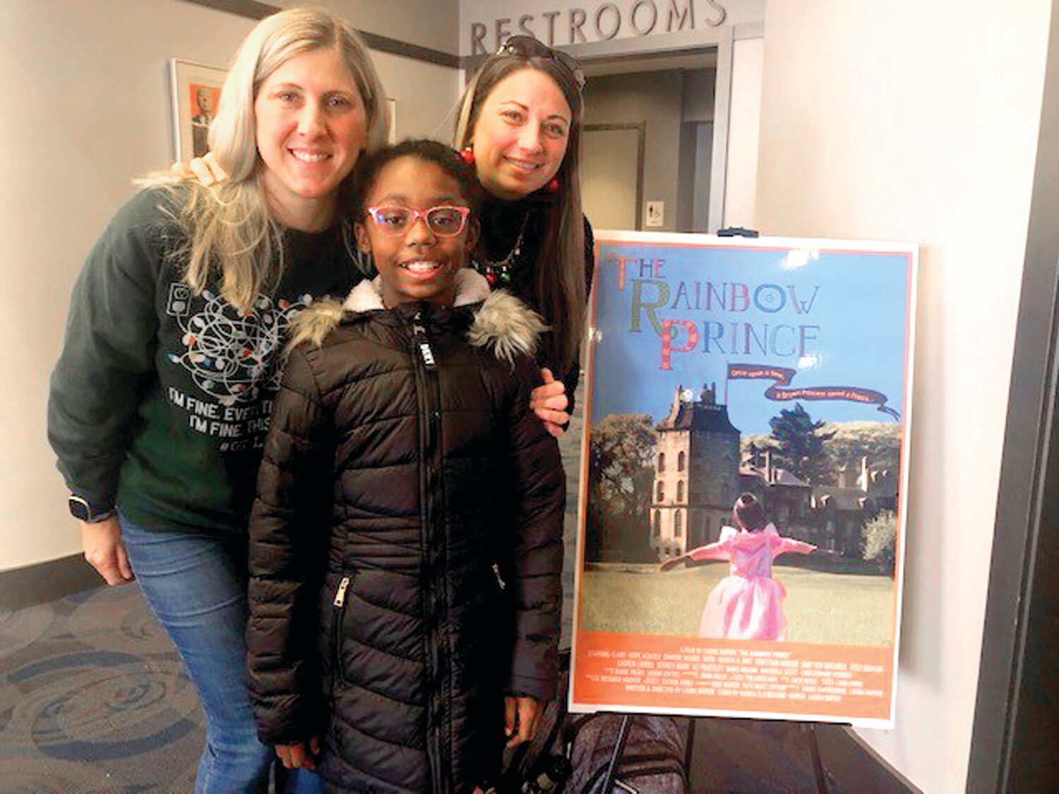 Junior Girl Scout, Marea, center, co-wrote and illustrated “The Rainbow Prince,” a modern fairy tale with her mother that was shown at the County Theater in Doylestown in December,  takes a moment with her troop leaders, beside the film’s poster.