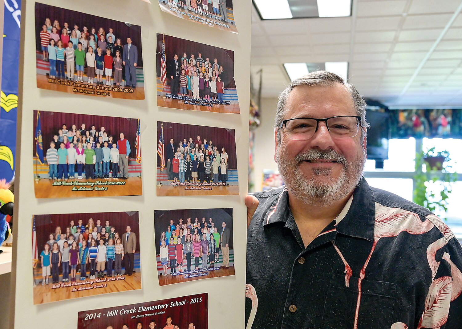 Jim Molenari stands beside a wall displaying class pictures from his years in Central Bucks.