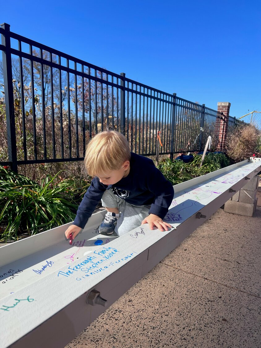 A young child adds to a signed beam for the new Children’s Village.