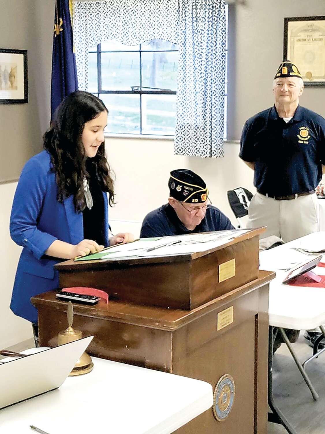 Mila Acosta-Morales reads her state award-winning essay, as American Legion Post 210 Adjutant Ed Lisowski and Commander Pete Scott listen.