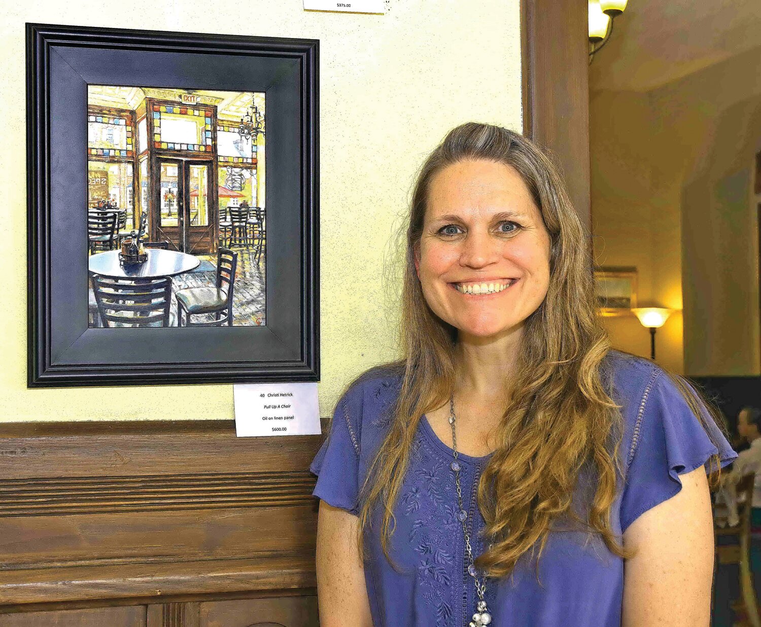Christi Hetrick next to her oil on linen panel, “Pull Up a Chair.”