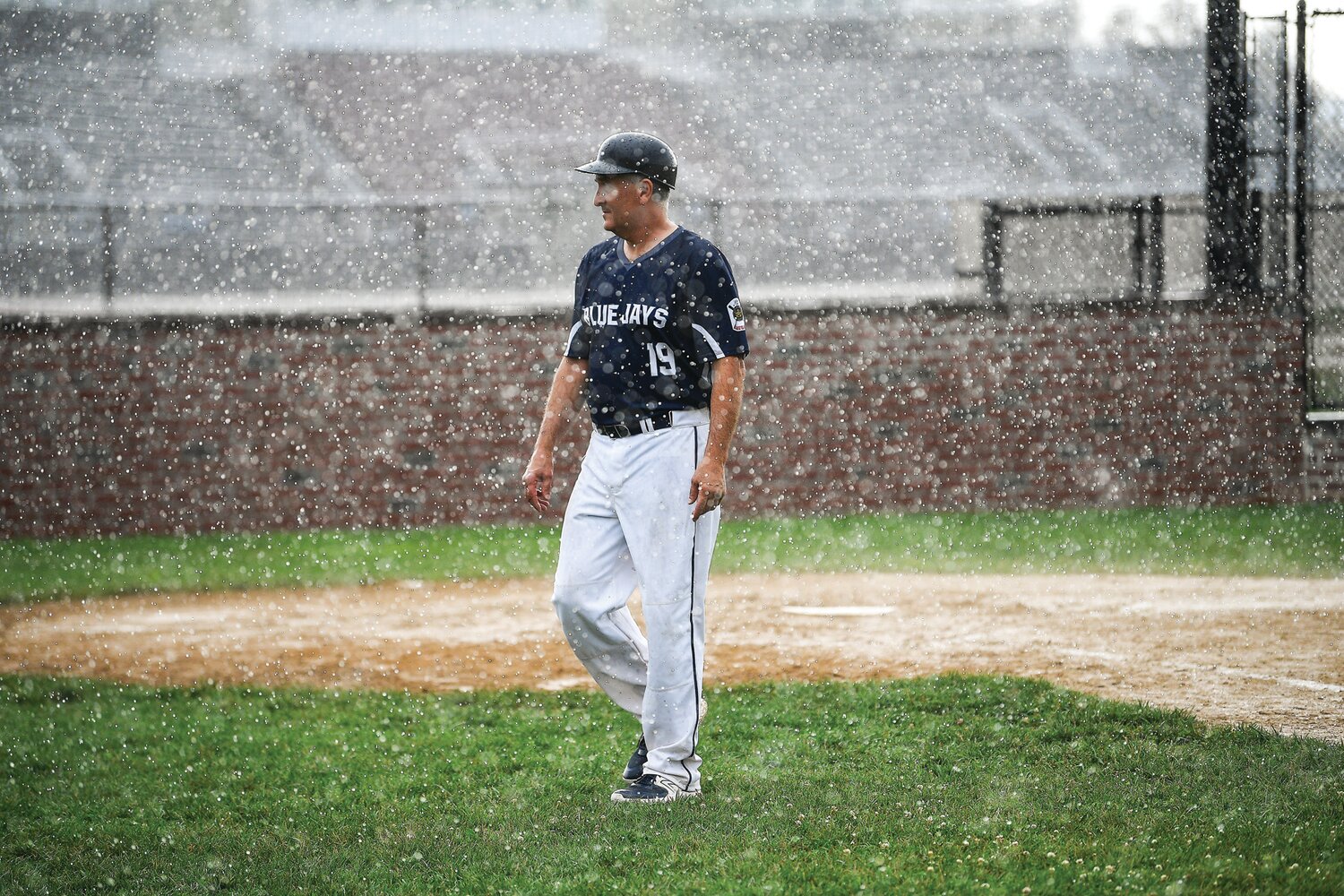 Quakertown manager Bob Helm casually walks off the field as the storm intensifies, resulting in a suspended game at 0-0 in the bottom of the second inning Monday. The game was resumed Wednesday night.