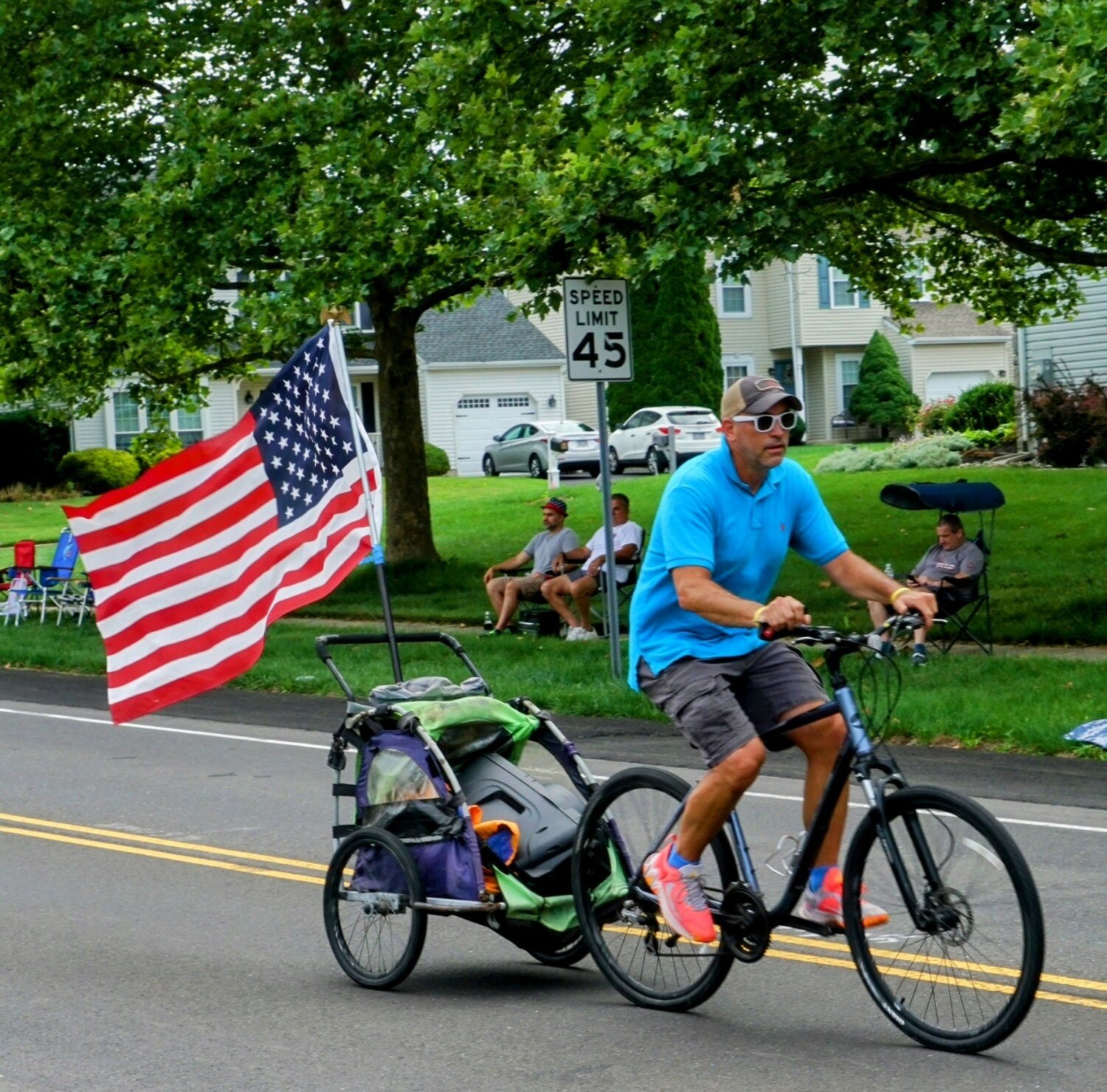 Tim McAnany, of Chalfont, cycles through town towing an American flag during the Tri-Municipal July 4 Parade.