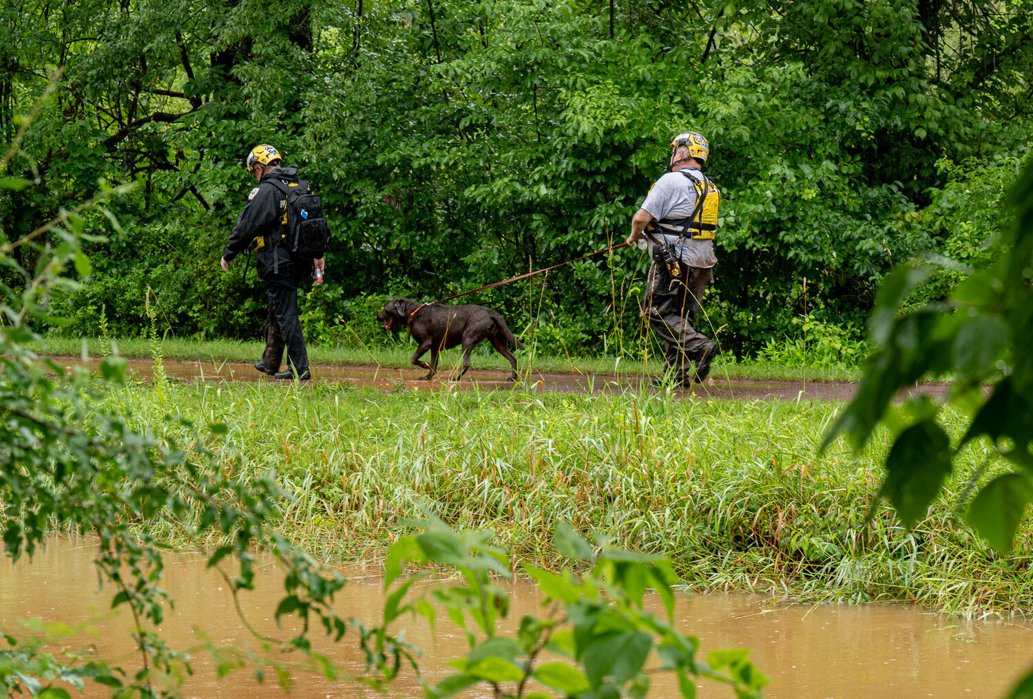 Two first responders, along with their dog, search along the canal Sunday. Five people were confirmed dead in the Upper Makefield flash flood, but two children were still missing Sunday.