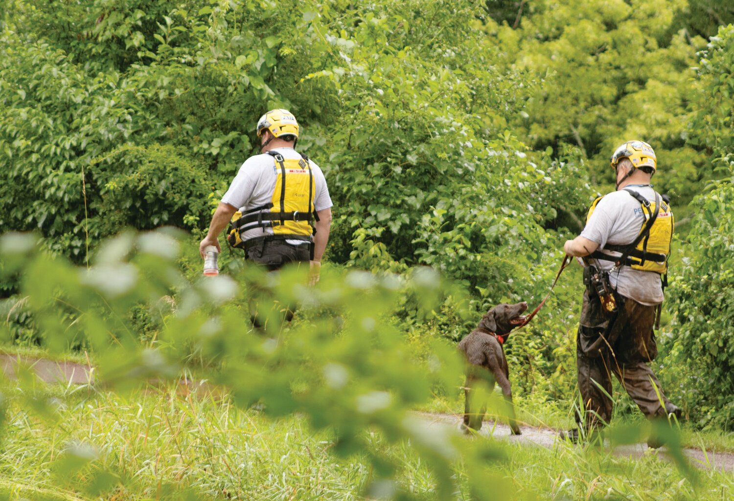 Two first responders, along with their search and rescue dog, search along the canal Sunday. Five people were confirmed dead in the Upper Makefield flash flood, but two children were still missing at press time.