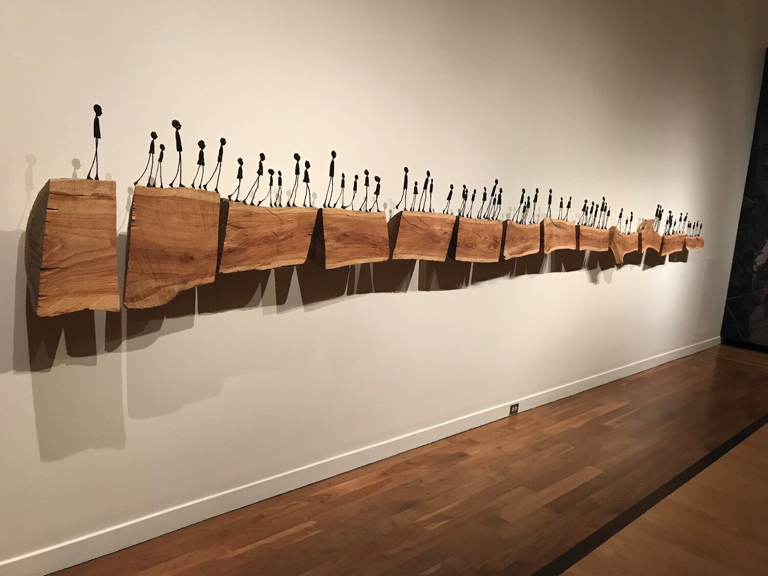 In “Bloodline” by Holly Wilson bronze figures cast from cigars and found sticks traverse a cut locust tree that fell down in a storm. The artist created the work after documenting her family ancestry in order to enroll herself and her children as tribal members.