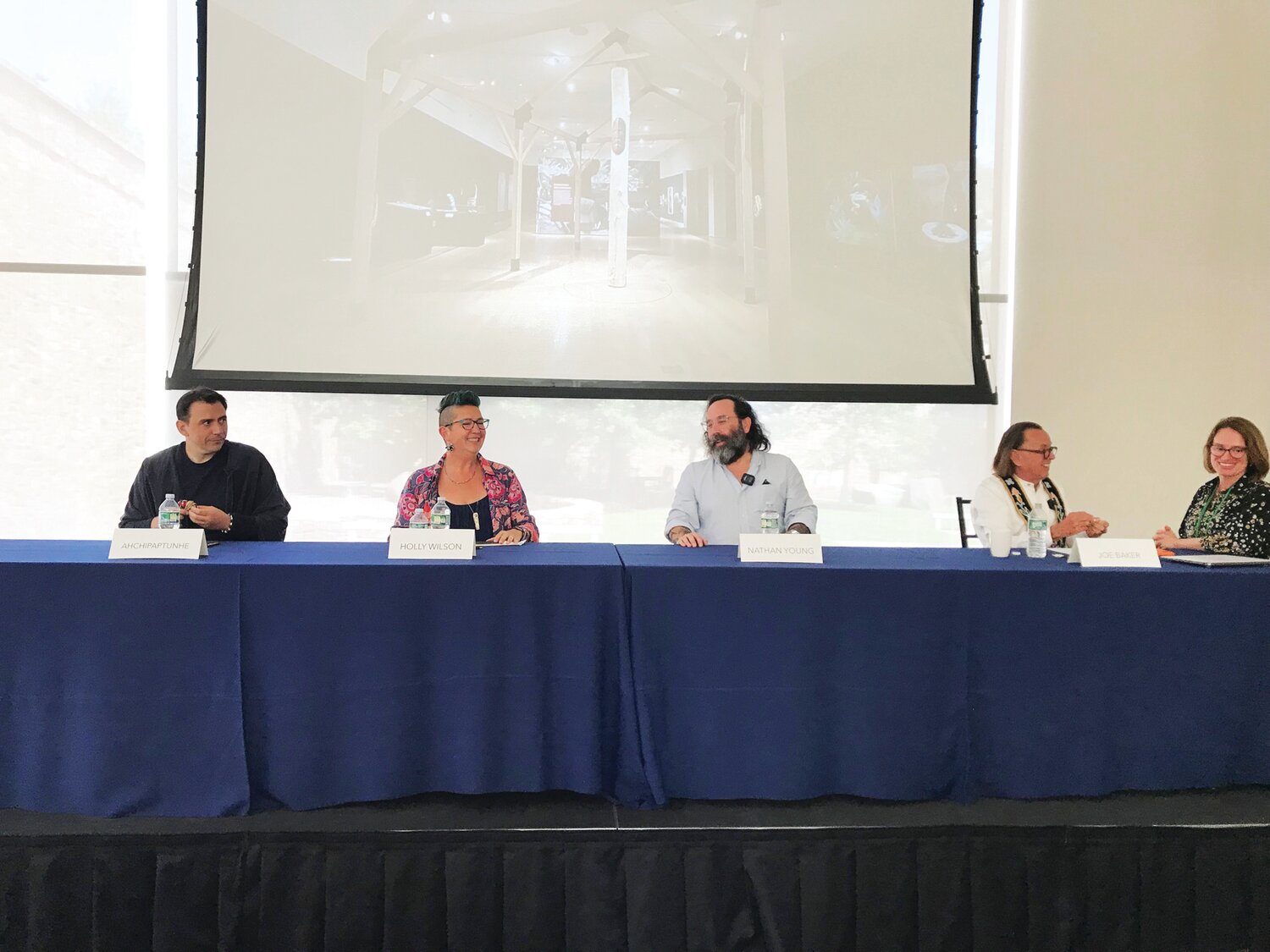 From left, during a panel discussion, are: Ahchipaptunhe, Holly Wilson, Nathan Young, Joe Baker and Laura Turner Igoe. On the screen above them is a photo of a potion of the “Never Broken” exhibition's Big House.