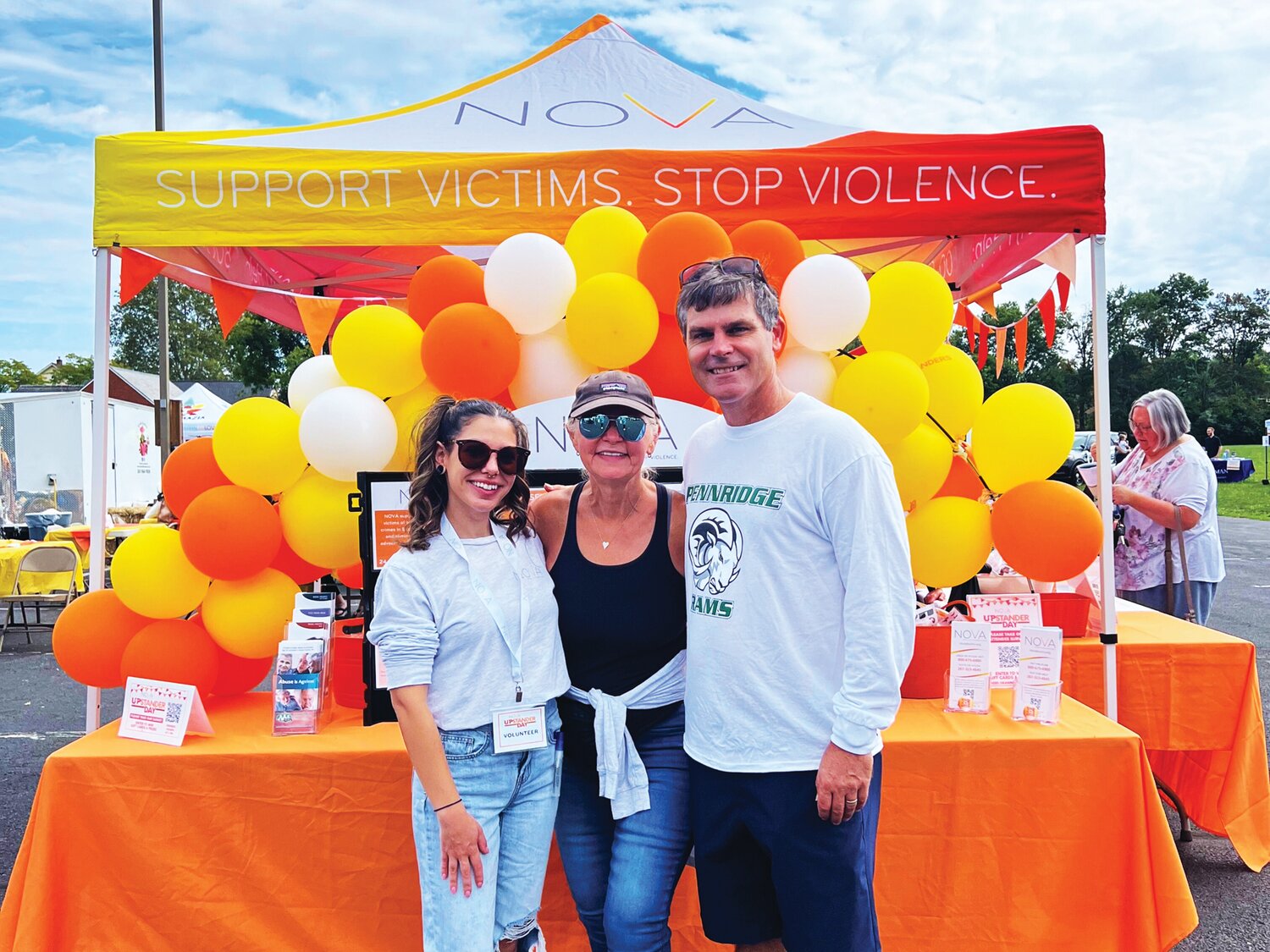 NOVA High School Primary Prevention Coordinator Katie Sanford and NOVA Director of Prevention and Training Mary Worthington pose in front of NOVA’s tent with Joseph Werner, Pennridge High School social worker.