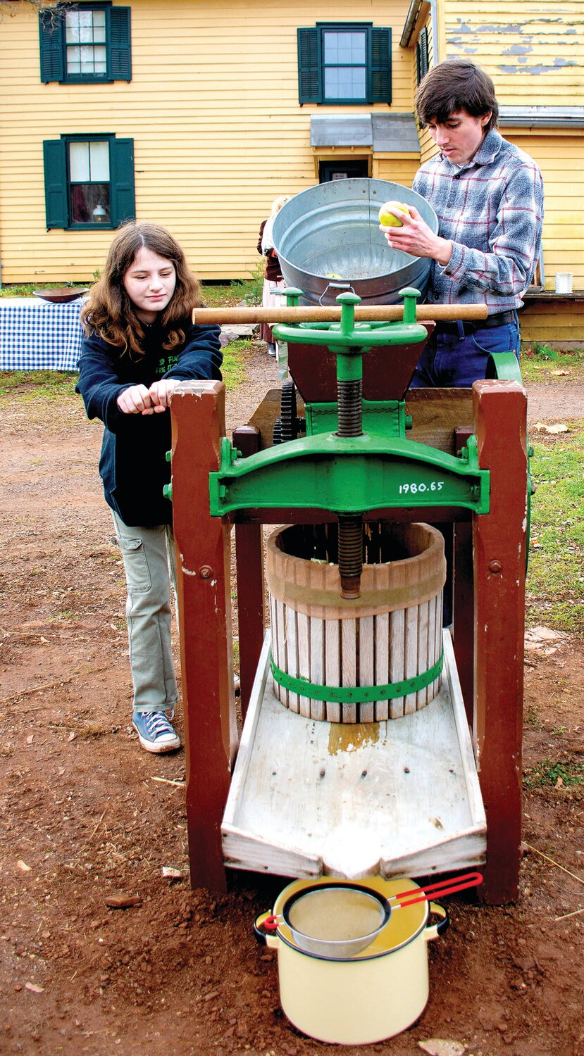 Visitors crank the apple cider press and add apples to the hopper at Howell Living History Farm.