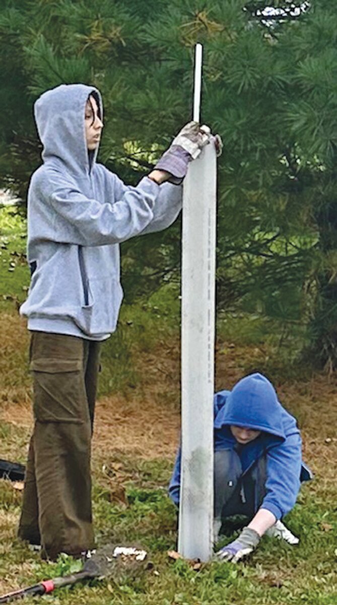 Volunteers encase a tree in a white plastic tube to protect it from deer.