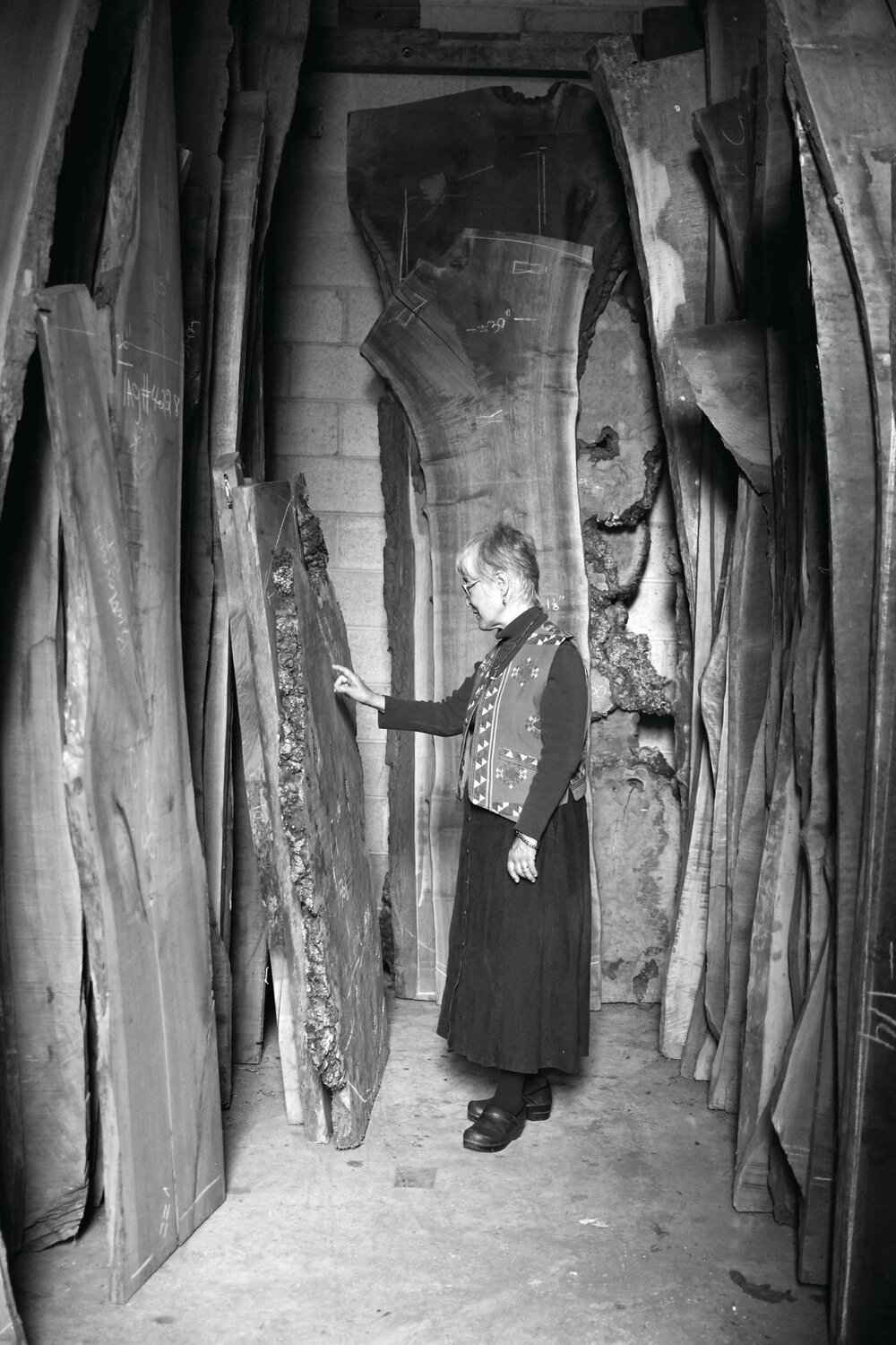 Mira Nakashima stands among the inventory of wood slabs stored as future furniture to be built by studio craftsmen.