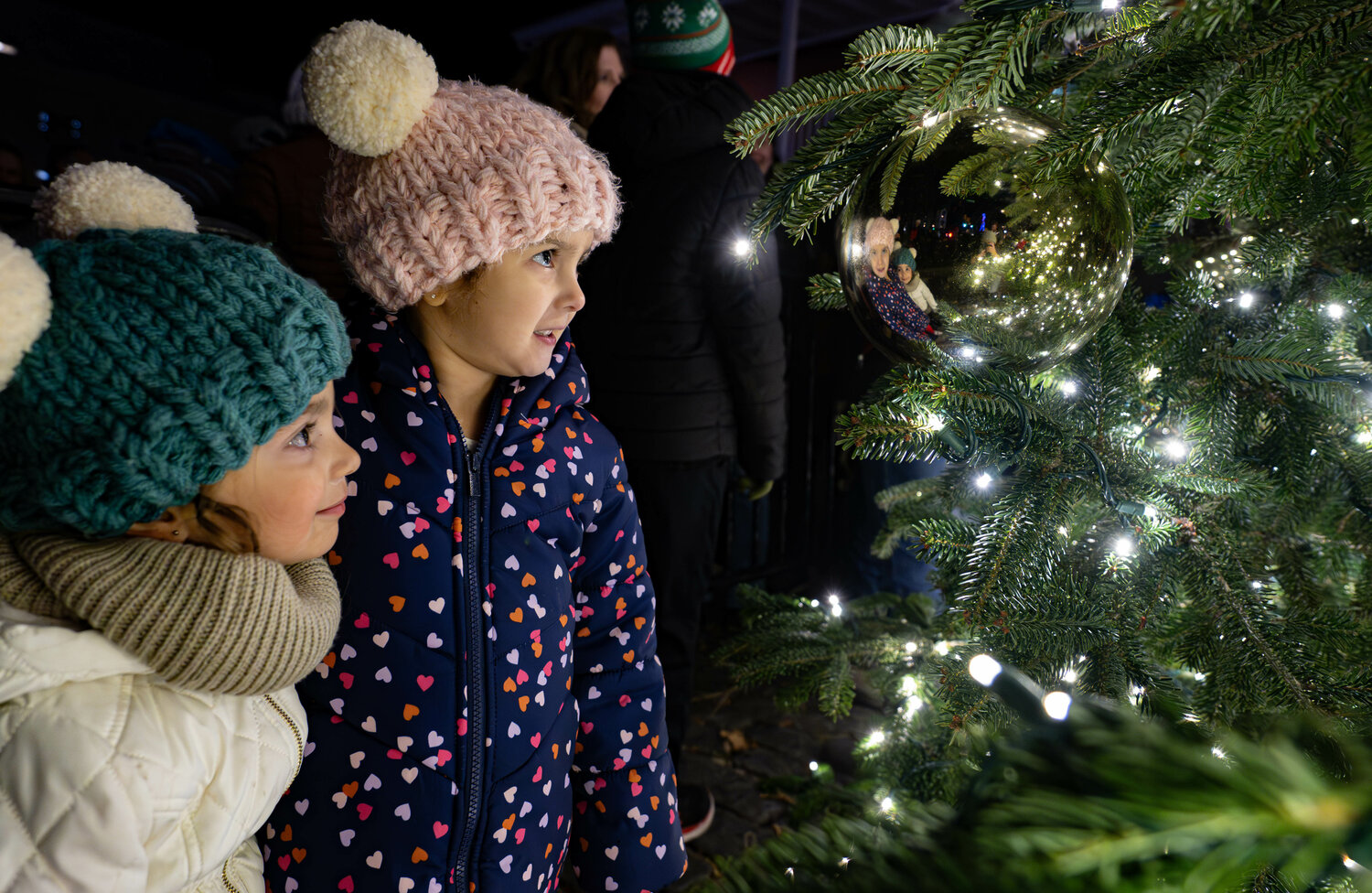 Amelia Millstein, left, and Florence Millstein marvel at their reflection in a Christmas ornament hanging from the newly lit Christmas Tree at the Doylestown Borough Christmas Tree Lighting event Friday night.