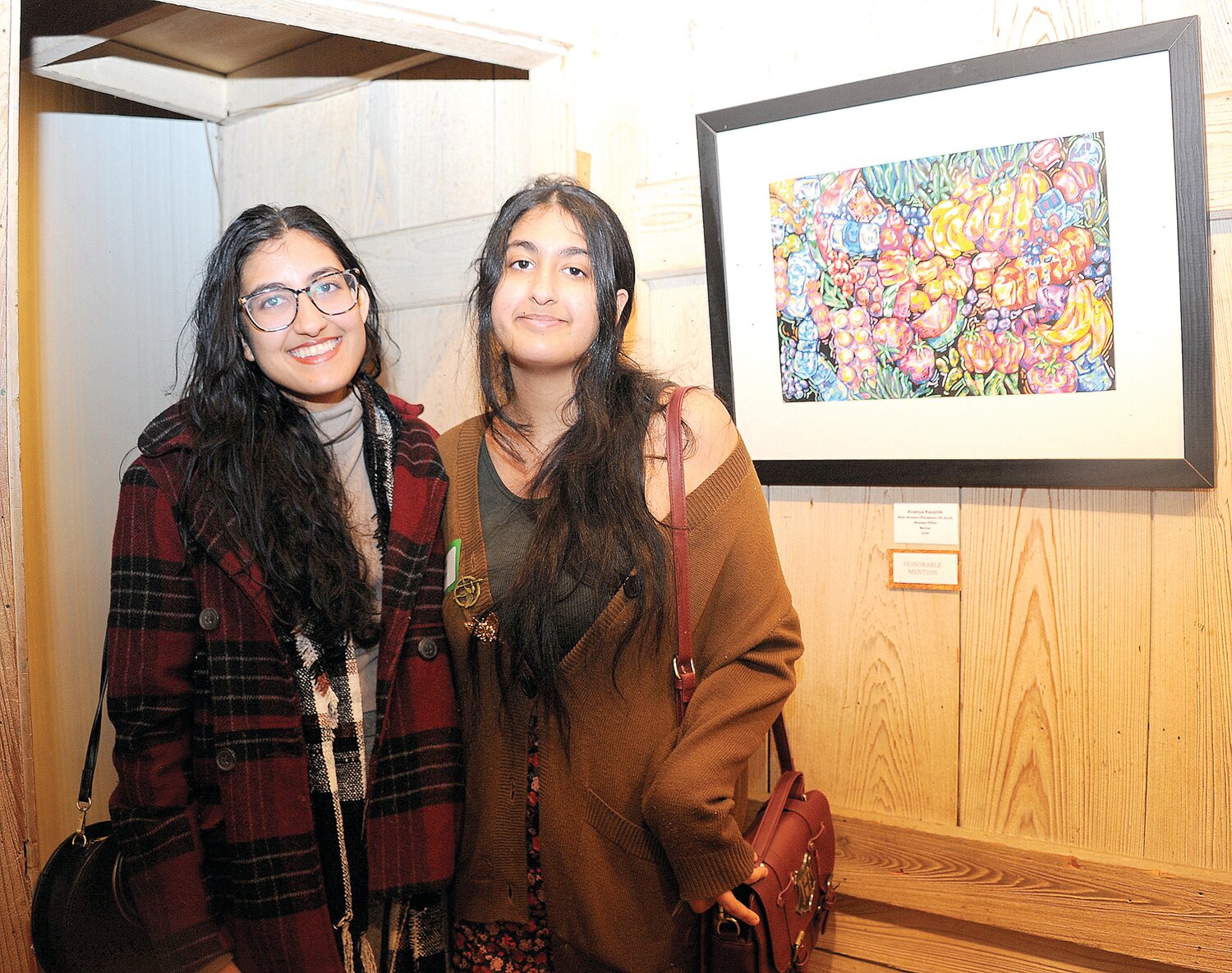 Ajita and sister Ananya Kaushik stand next to Ananya’s honorable mention painting “Wasted Effort.”