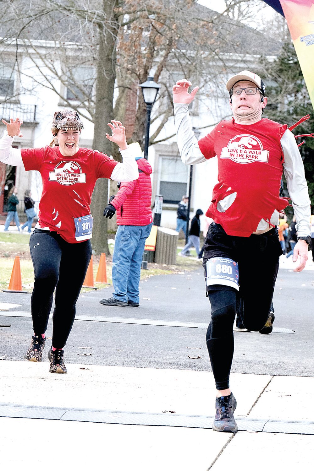 Melissa Showalter, wearing a dinosaur hat, chases her fiance, Kevin Ruhf, across the finish line during the Great Cupid Run, an event he organized. Proceeds raised from the day go to the Bucks County Opportunity Council.