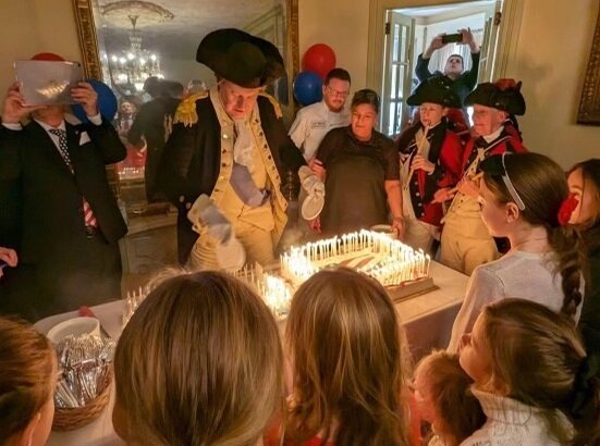George Washington, portrayed by Langhorne Borough Police Chief John Godzieba, cuts a birthday cake containing 292 candles as children and veterans look on.