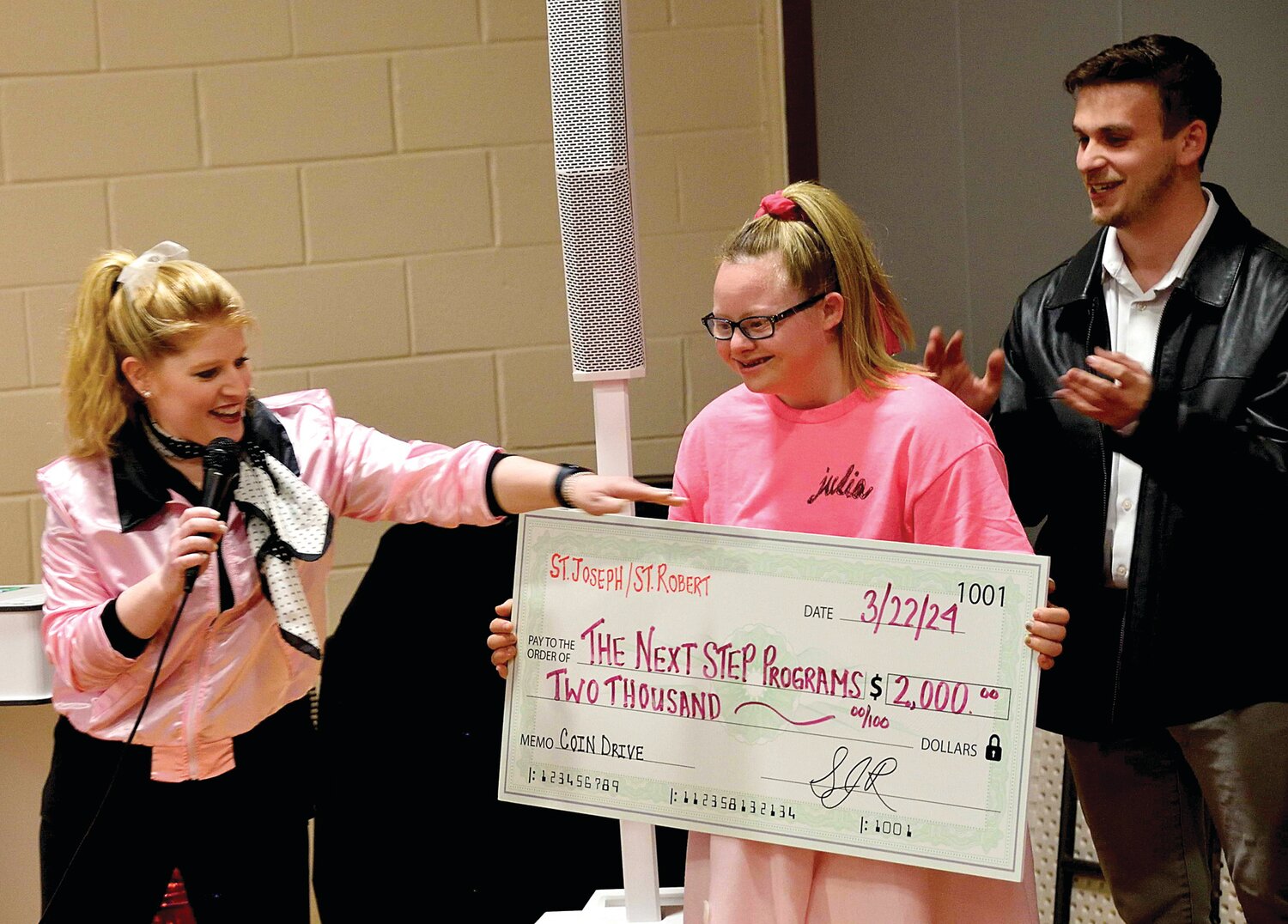 St. Joseph/St. Robert Home and School Association President Nikki DeGuida presents the check to The Next Step's Julia Shirey, while Josh Fields, The Next Step executive director, applauds.