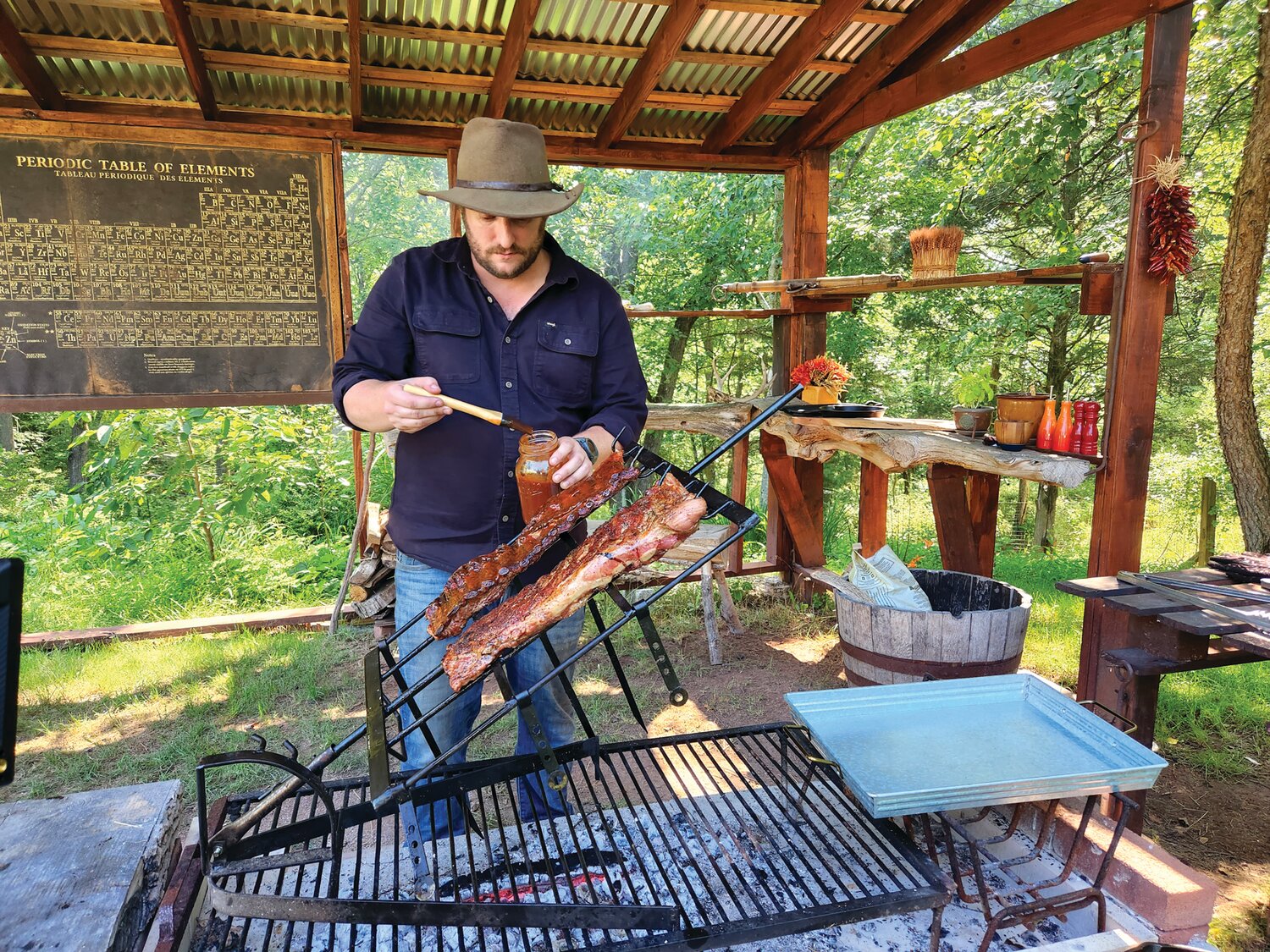 Thor Giese applies barbecue sauce to a rack of ribs cooking over the coals.