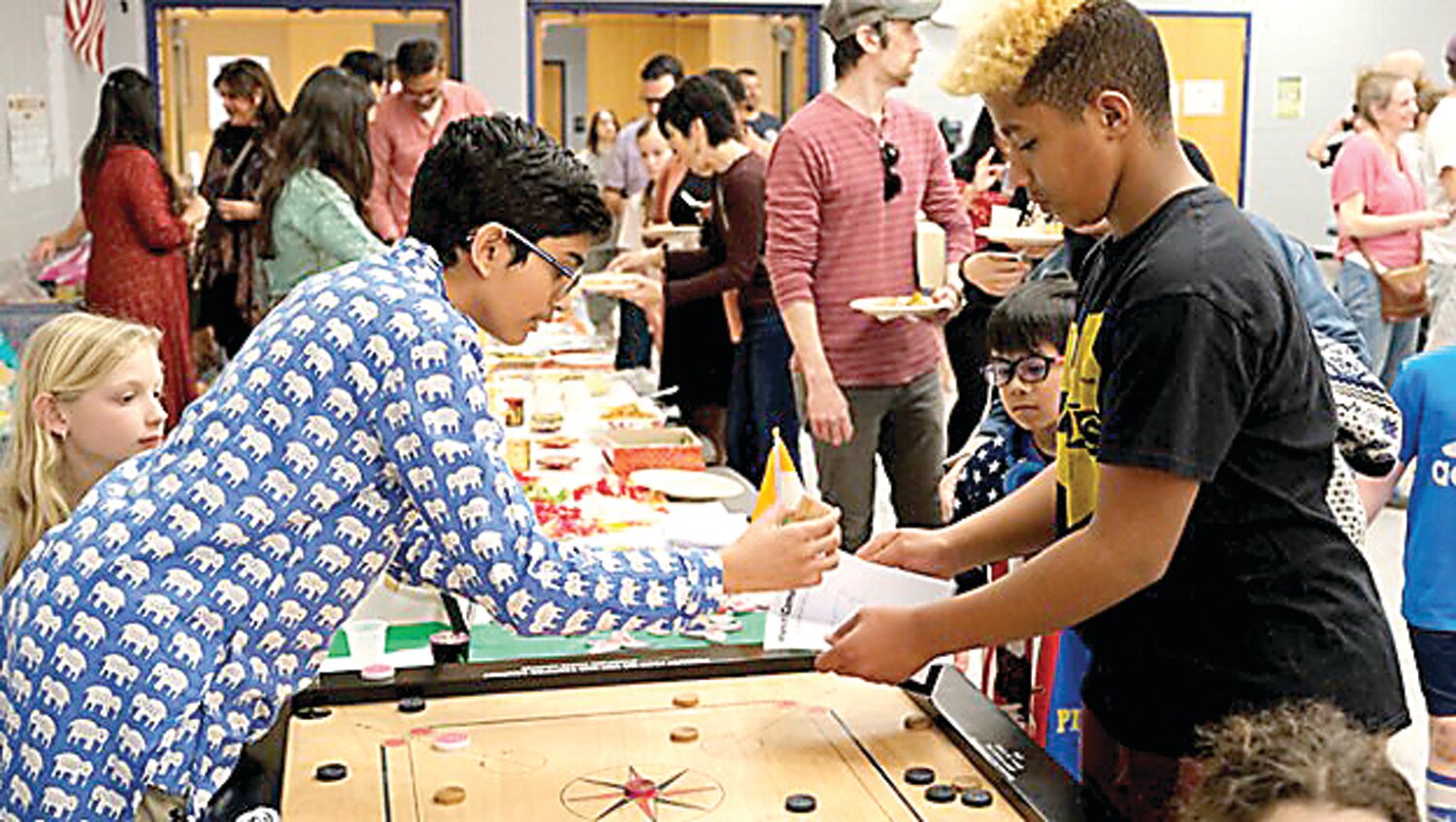 New Hope-Solebury student Mohneesh Vinukollu demonstrates how to play Carrom and helps fill in a passport book for fellow student Ethan Tumminello.