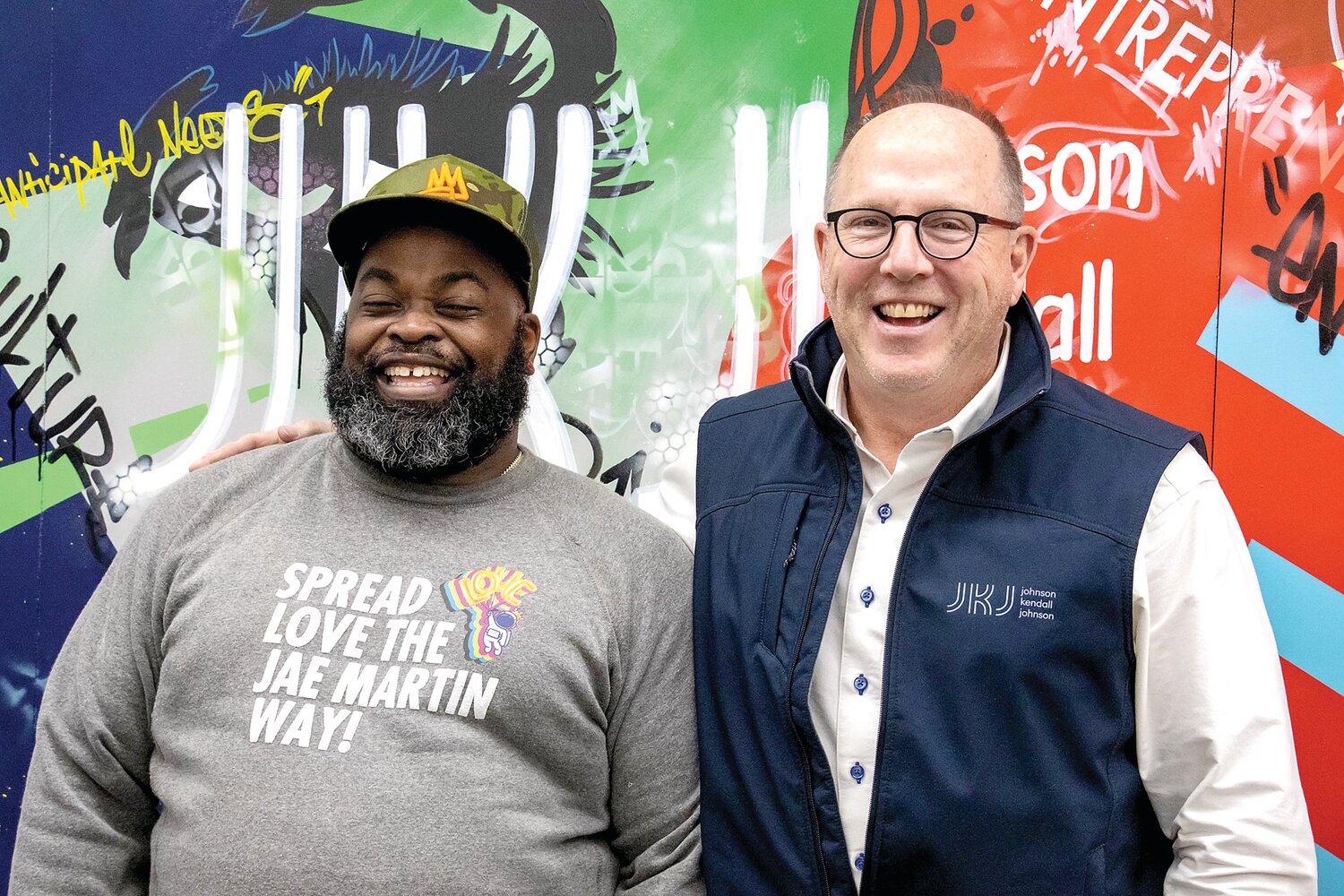 Pop artist Jae Martin, left, and Bruce White, CEO of Johnson Kendall & Johnson, stand in front of the feature wall Martin created for the independent insurance brokerage and risk management firm in Newtown.