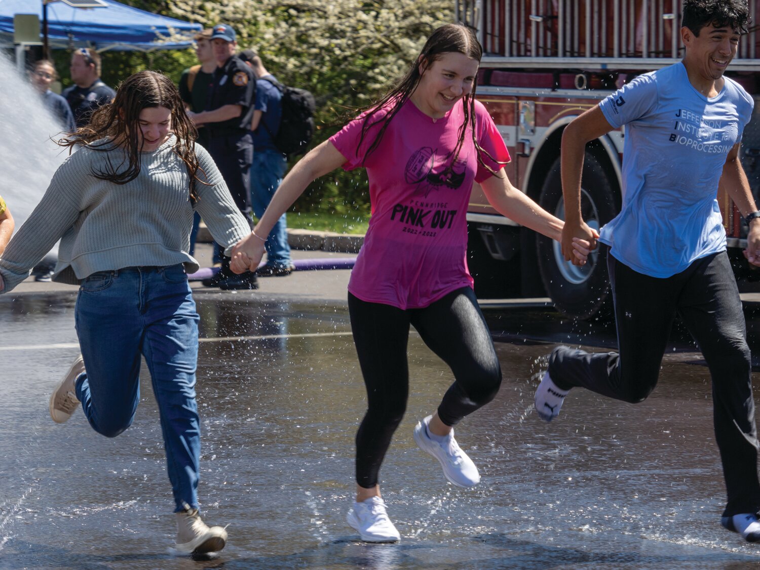 Students hold hands as they run through a deluge of water.
