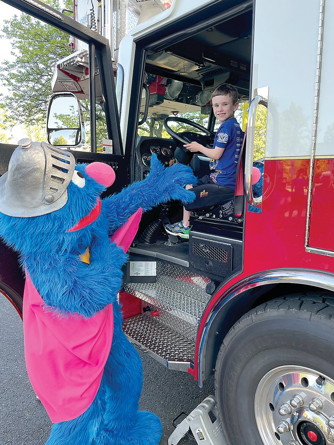 Seven-year-old Jackson Bucantis sits in the driver’s seat of the Langhorne-Middletown Fire Company’s 21 Truck and makes friends with Sesame Place character Grover during a recent visit. Kids participating in the Kiwanis-Herald Sesame Place Classic races on May 19 will get a chance to do the same.