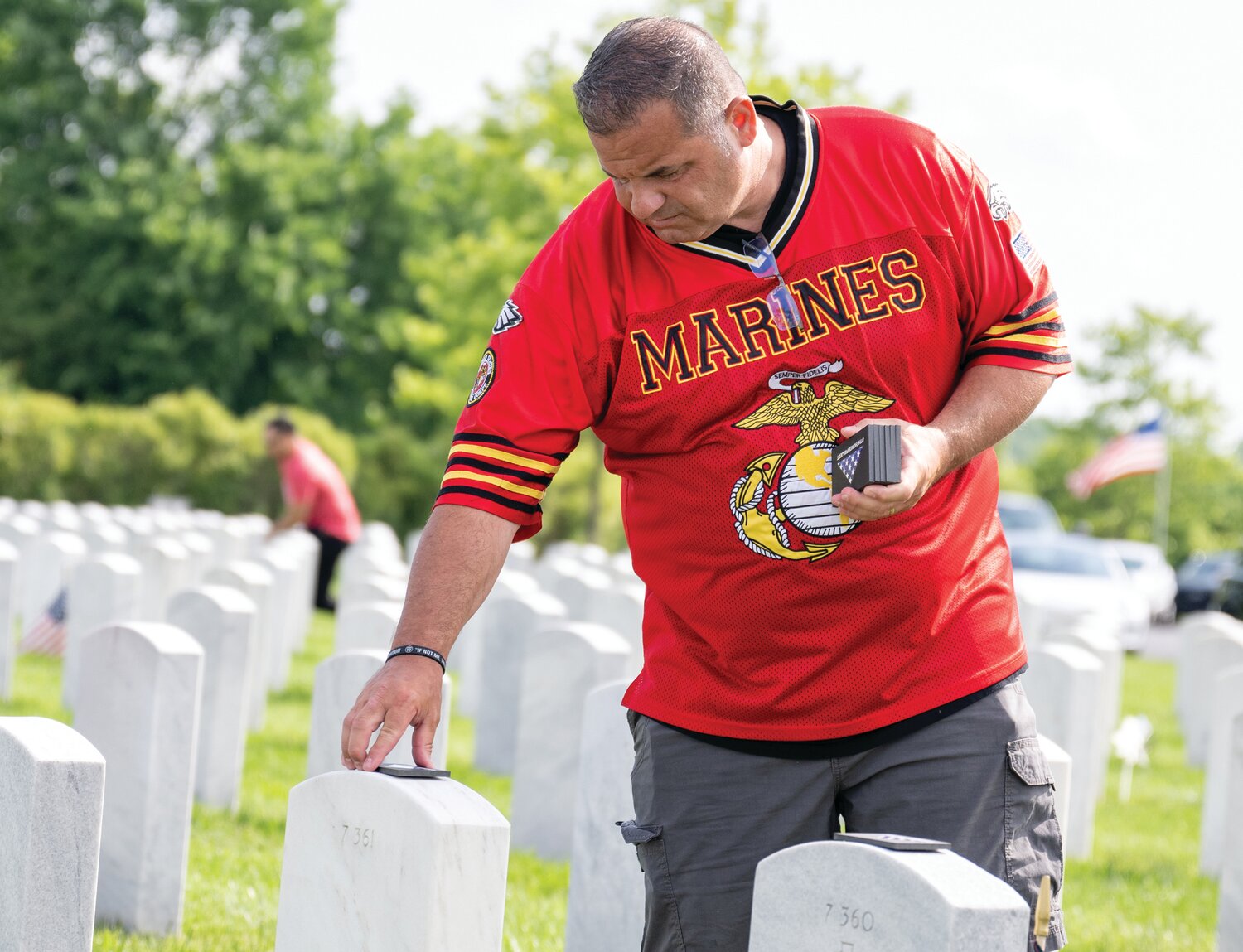 A volunteer participating in The Honor Project places a commemorative token on the gravestone at Washington Crossing National Cemetery.