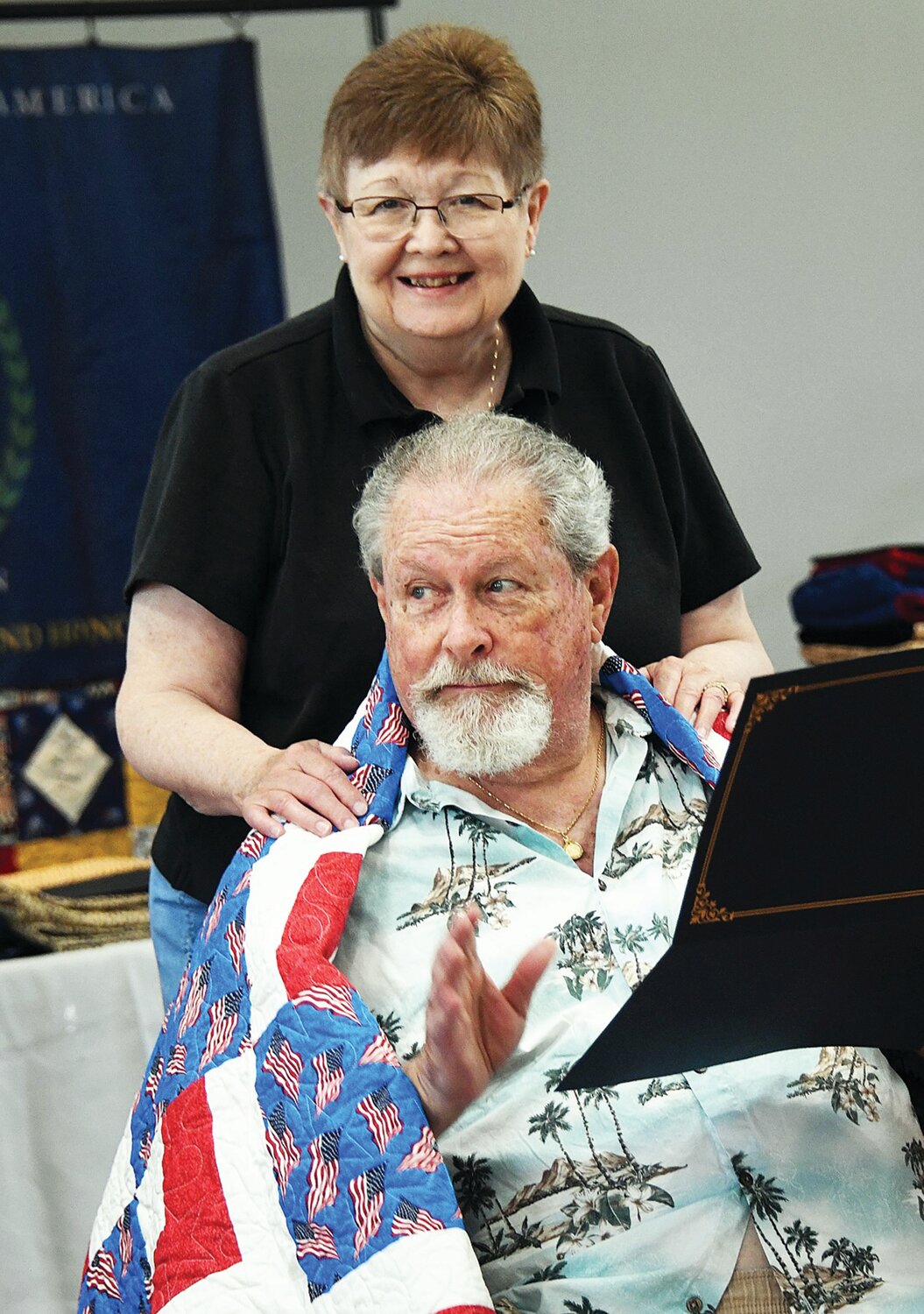 John Snyder, with his wife, is wrapped in a quilt given by the Quilts of Valor.